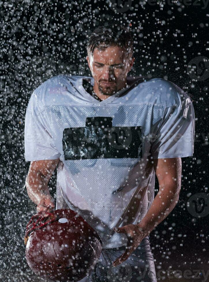 américain Football champ solitaire athlète guerrier permanent sur une champ détient le sien casque et prêt à jouer. joueur en train de préparer à courir, attaque et But atterrissage. pluvieux nuit avec spectaculaire brouillard, bleu lumière photo