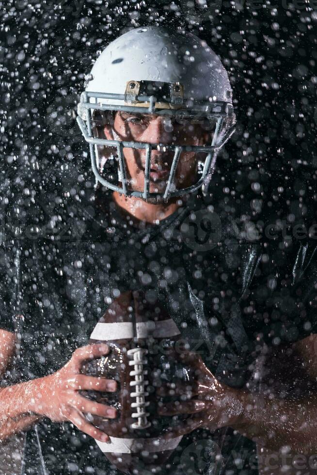 américain Football champ solitaire athlète guerrier permanent sur une champ détient le sien casque et prêt à jouer. joueur en train de préparer à courir, attaque et But atterrissage. pluvieux nuit avec spectaculaire brouillard, bleu lumière photo