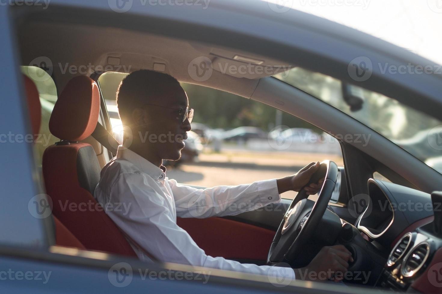 heureux afro-américain conduisant une voiture avec un téléphone, en été photo