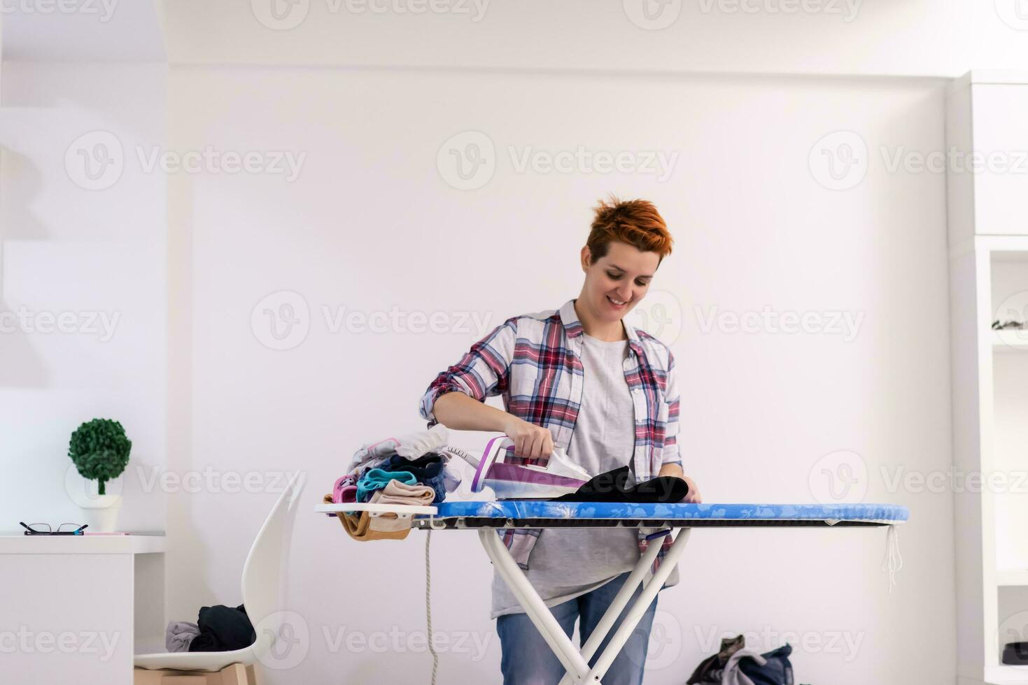 femme aux cheveux rouges repassant des vêtements à la maison photo