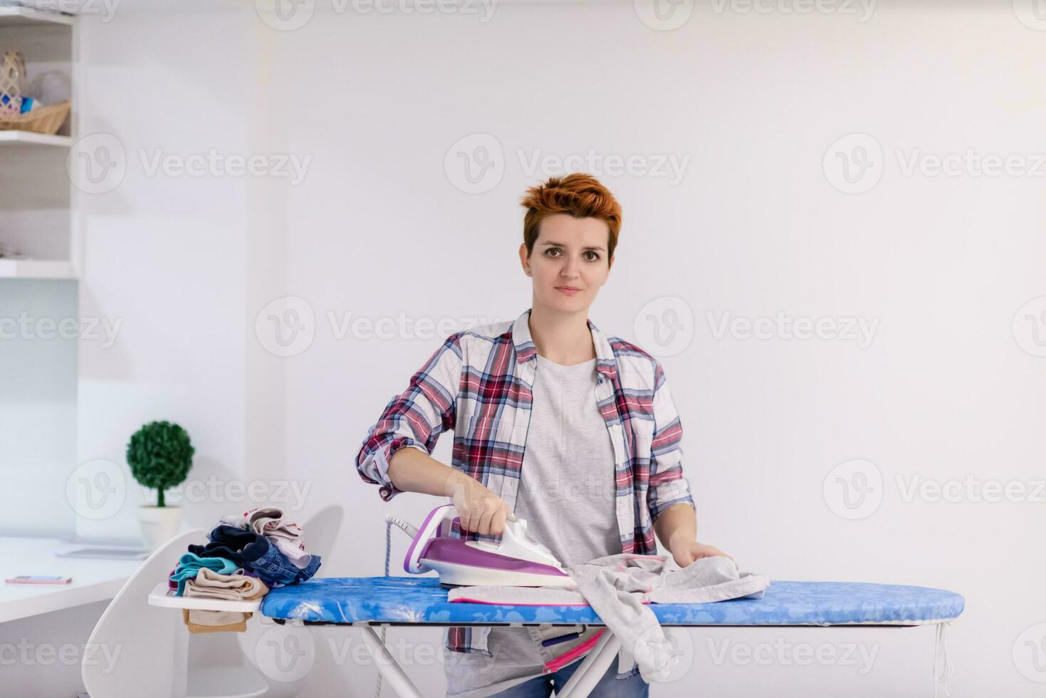 femme aux cheveux rouges repassant des vêtements à la maison photo