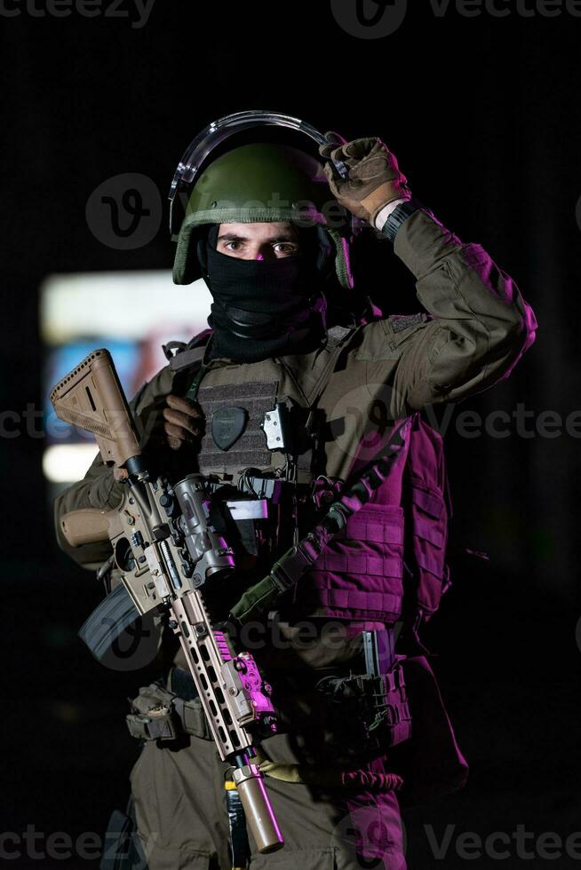 armée soldat dans combat uniformes avec un agression fusil et combat casque nuit mission foncé Contexte. bleu et violet gel lumière effet. photo