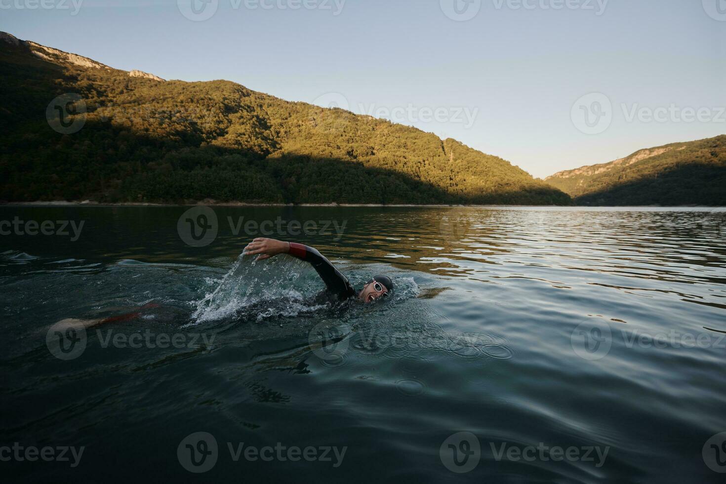 athlète de triathlon nageant sur le lac au lever du soleil portant une combinaison de plongée photo