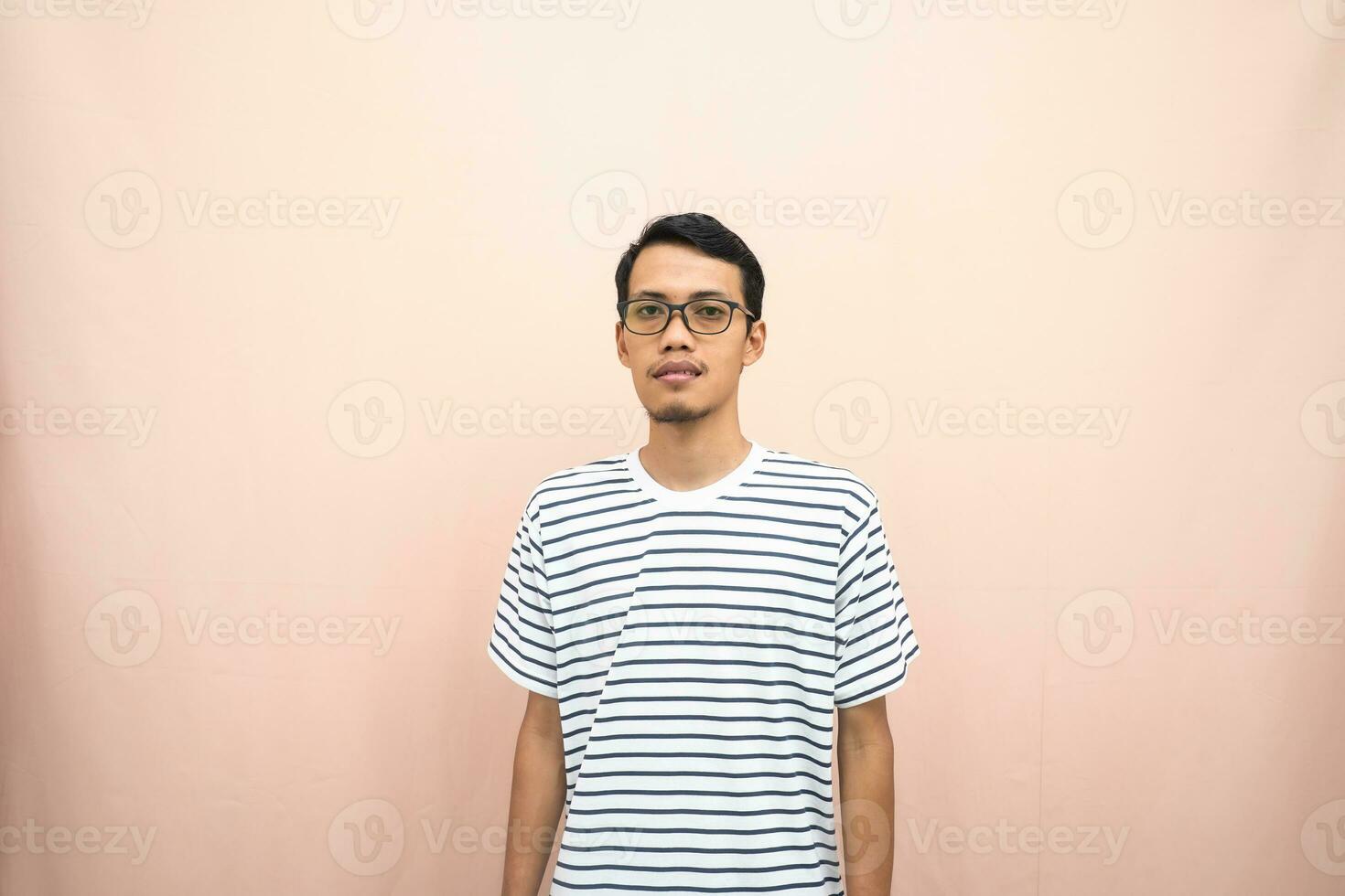 asiatique homme dans des lunettes portant décontractée rayé T-shirt, permanent pose, souriant et sérieux. photo