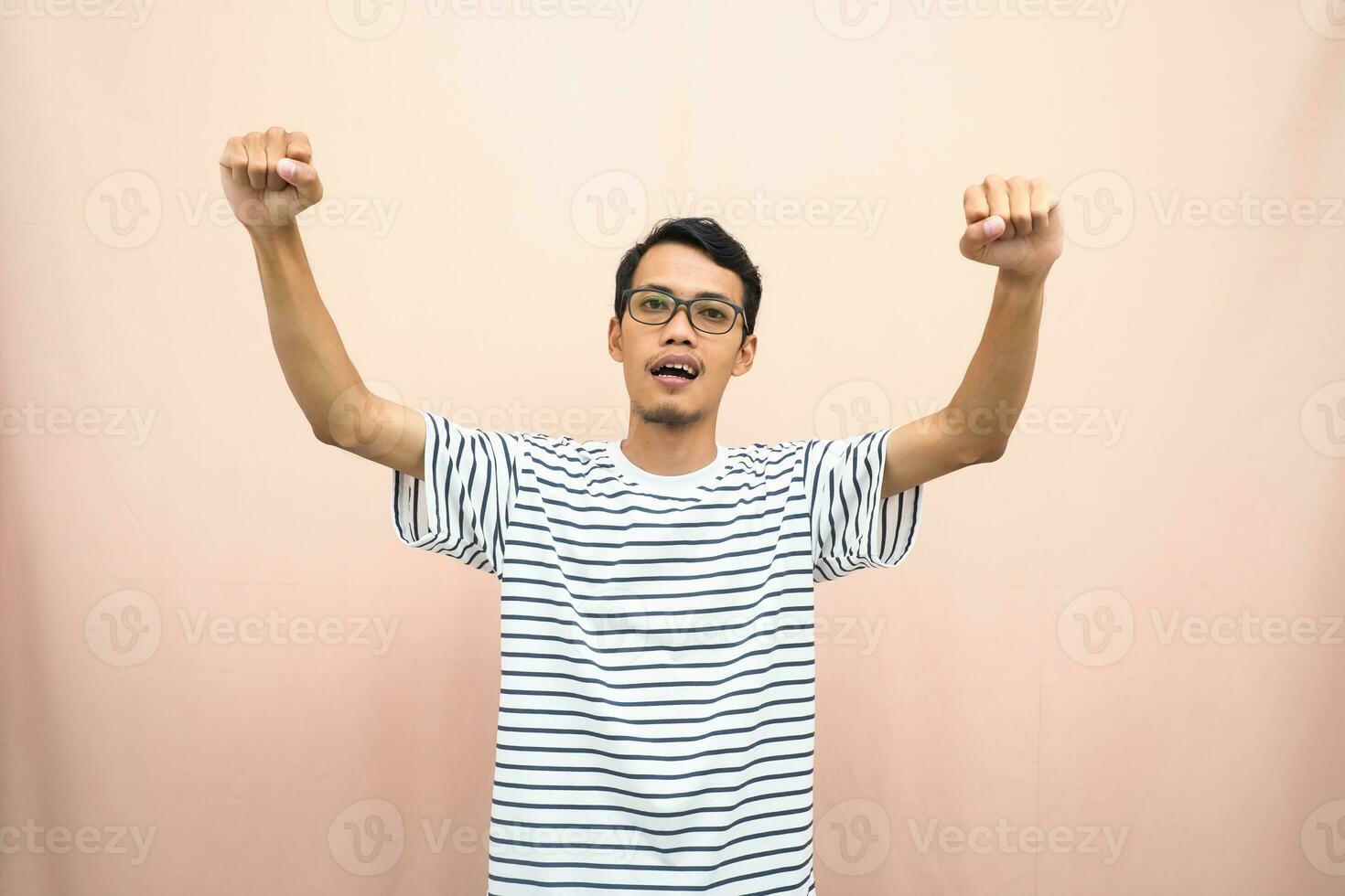 asiatique homme avec des lunettes portant décontractée rayé chemise, poing poing pose, indiquant fort ou prêt à lutte. isolé beige Contexte. photo