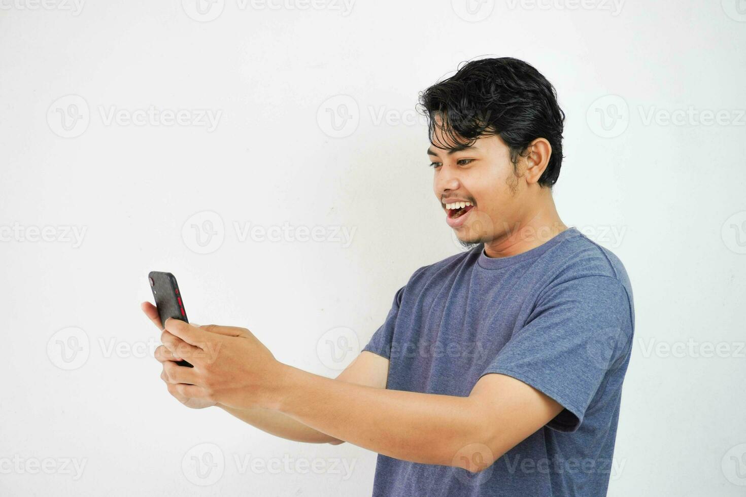 excité souriant ou content Jeune asiatique homme dans marine Couleur T-shirt en portant téléphone, isolé sur blanc Contexte photo