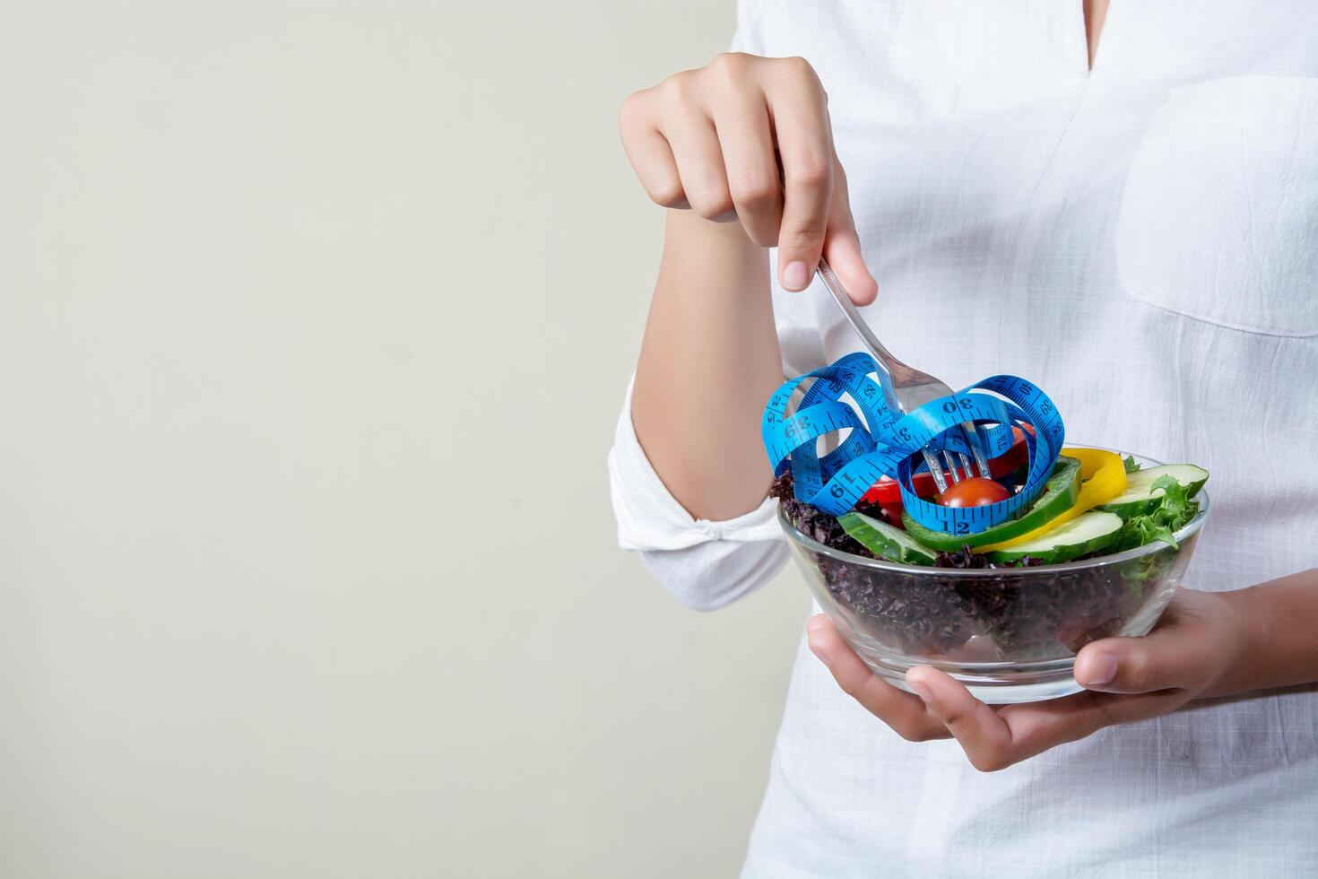 femme tenant une fourchette avec des légumes frais mélangés et un ruban à mesurer. photo