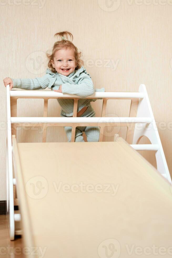 une peu fille grimpe une en bois faire glisser dans le salle de sport. le enfant va dans pour des sports et développe photo