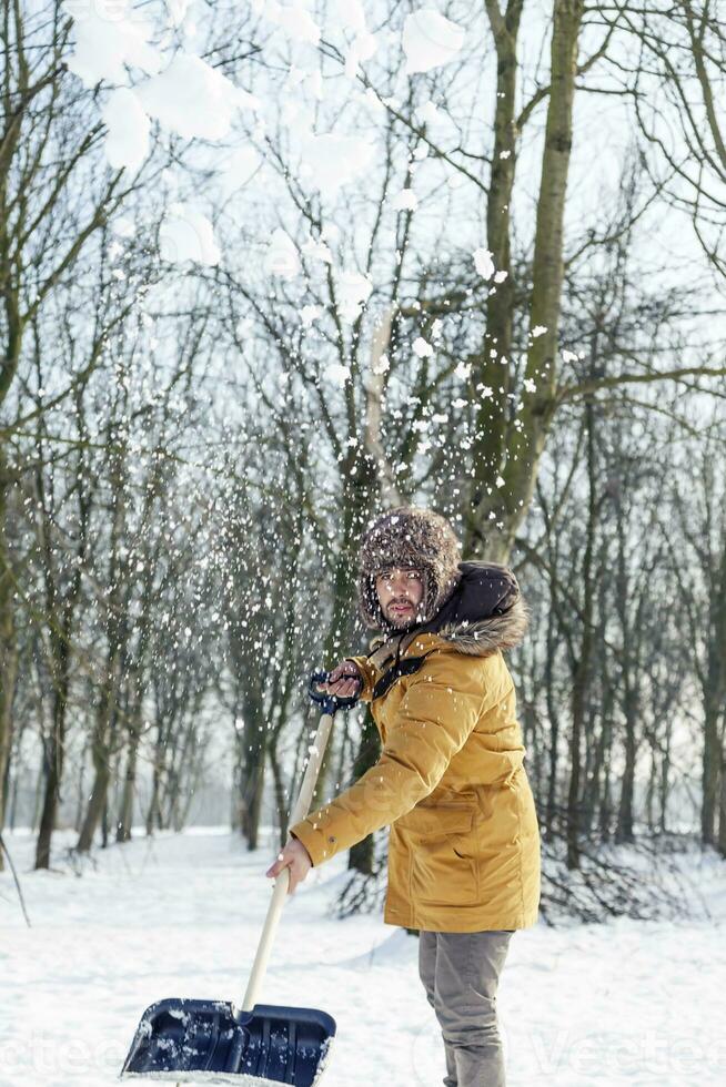 Jeune homme pelleter neige près une petit bois photo
