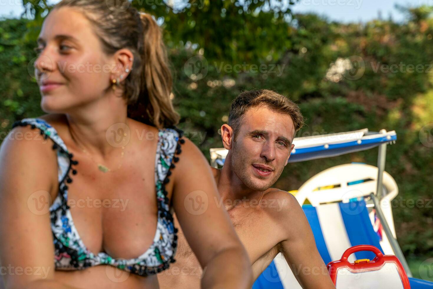 marrant portrait de Jeune Enceinte femme avec mari dans maillots de bain séance sur plage chaises photo