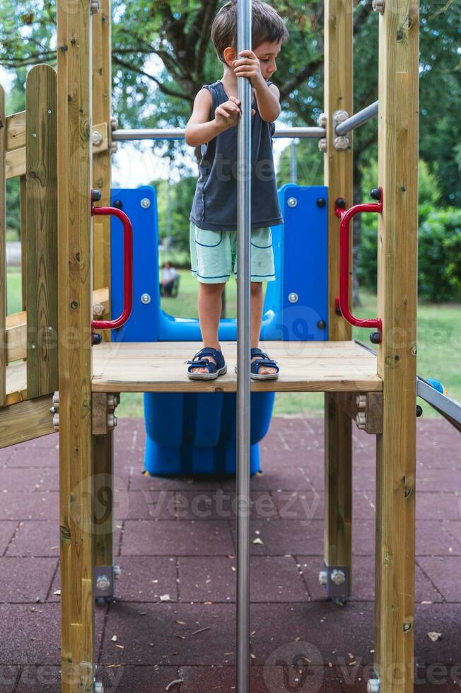 mignonne peu garçon avoir amusement escalade une en bois structure dans une terrain de jeux photo