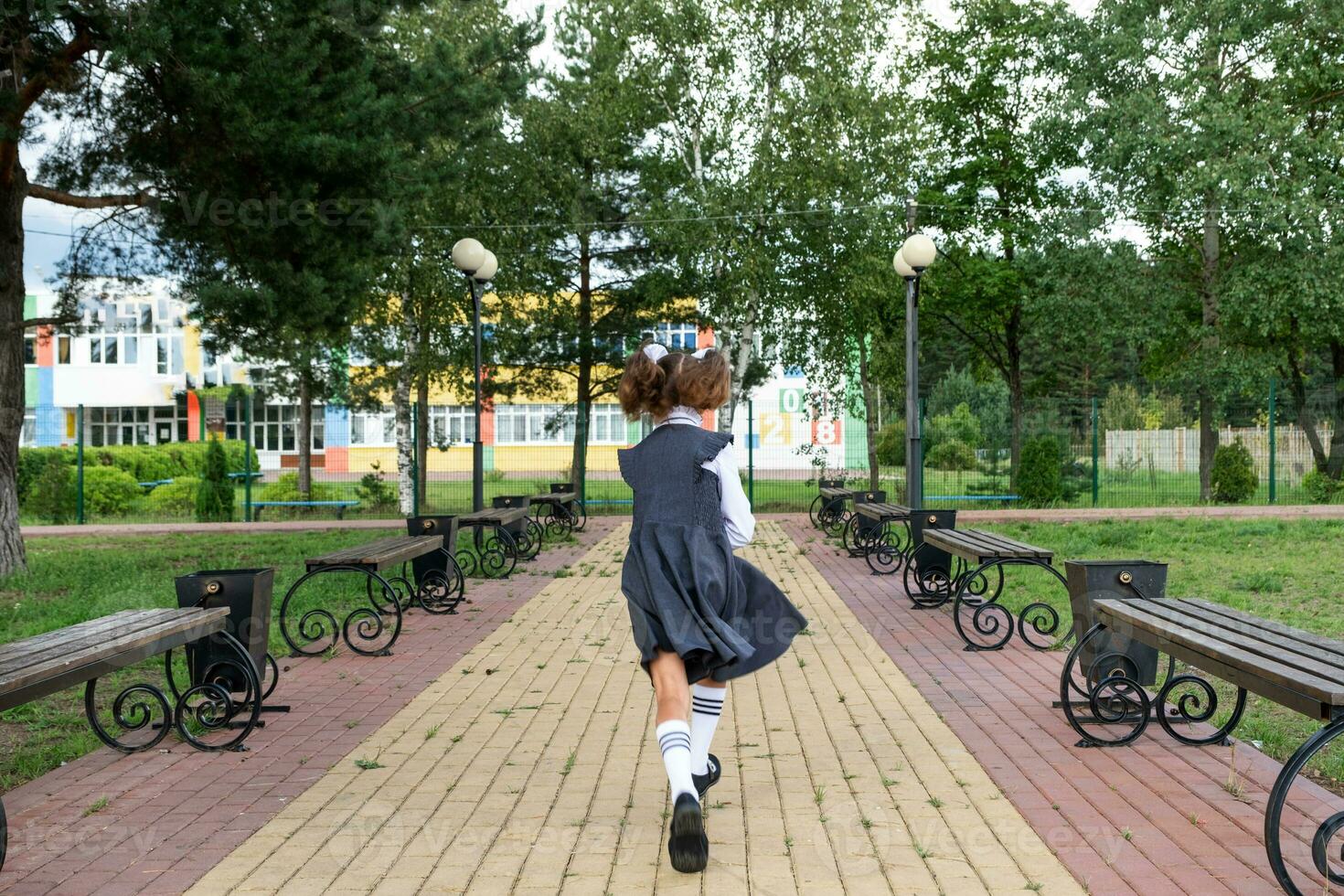 de bonne humeur marrant fille avec édenté sourire dans école uniforme avec blanc arcs fonctionnement dans école cour. retour à école, septembre 1. content élève avec sac à dos. primaire éducation, élémentaire classe. mouvement photo