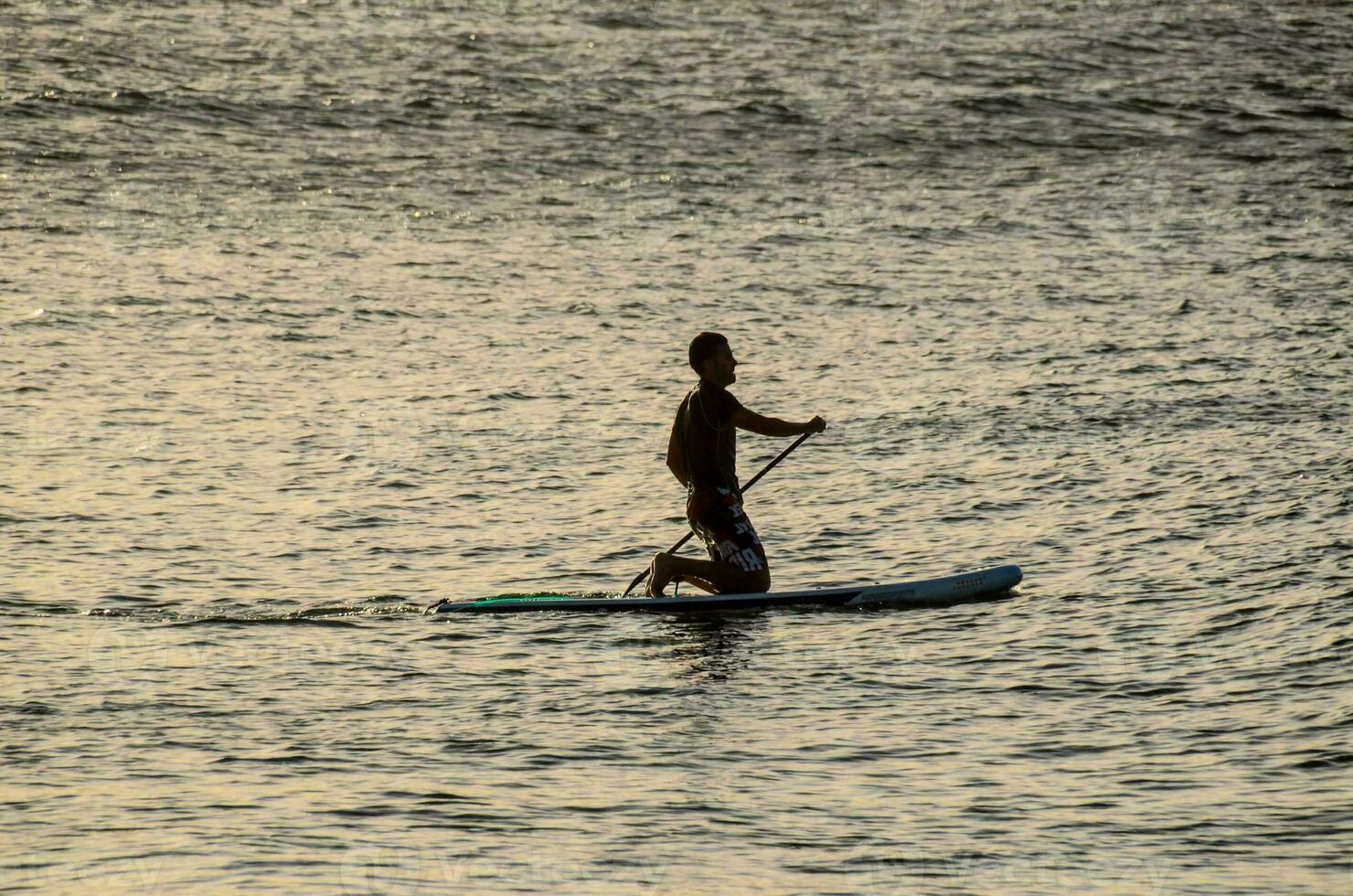 une homme est pagayer embarquement dans le océan à le coucher du soleil photo