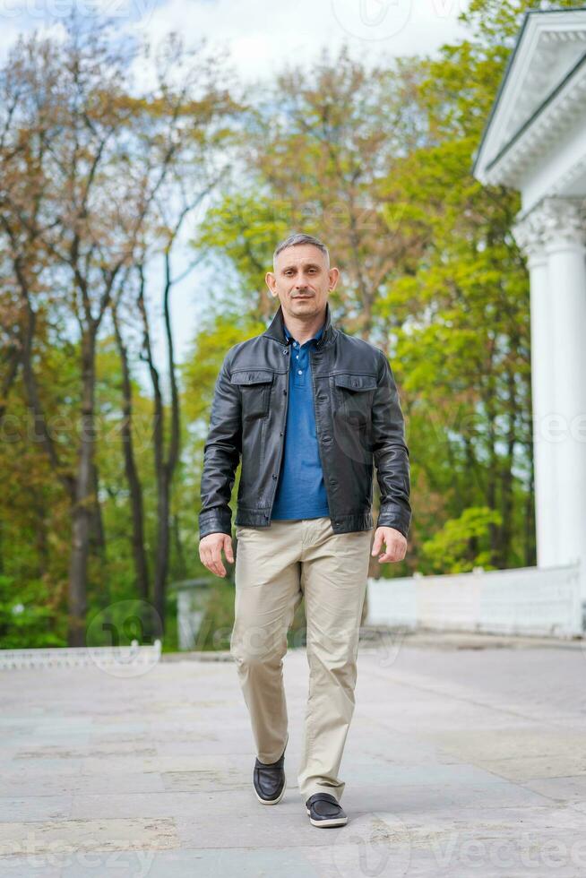 une homme dans décontractée vêtements des promenades près une magnifique bâtiment et regards à le caméra photo