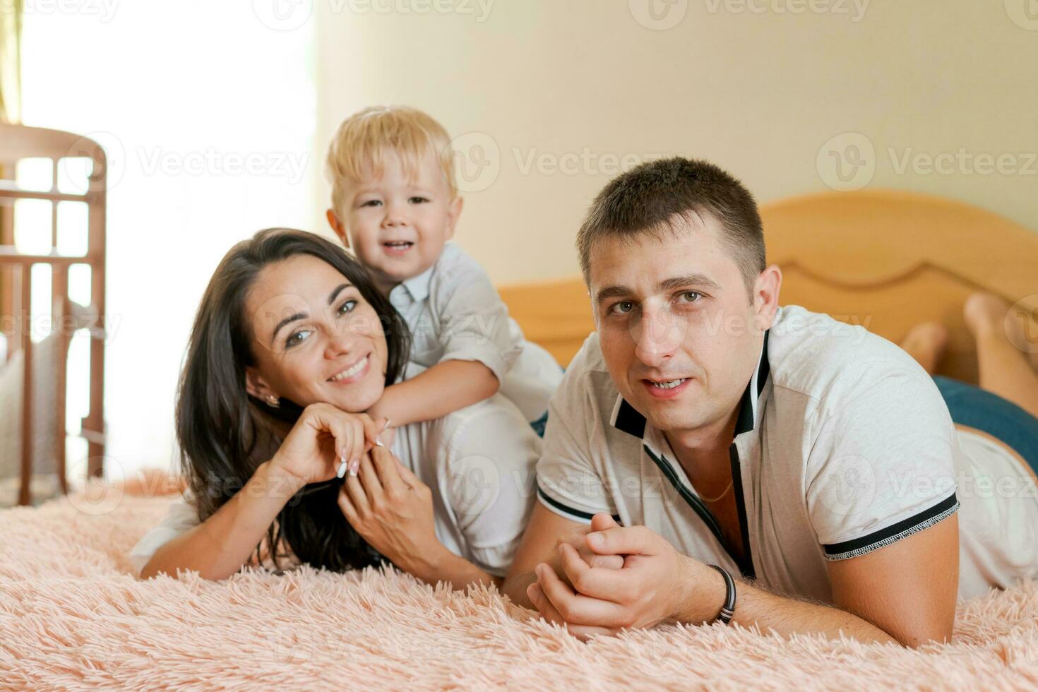 content famille mensonge sur le lit et étreindre, maman papa et peu fils photo