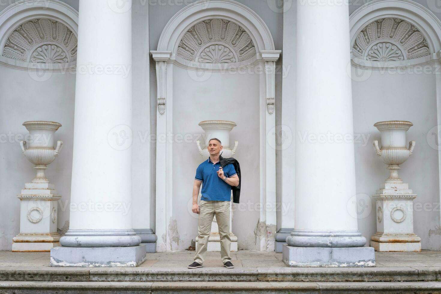 une homme dans décontractée vêtements des stands près le Colonnes de une blanc bâtiment photo