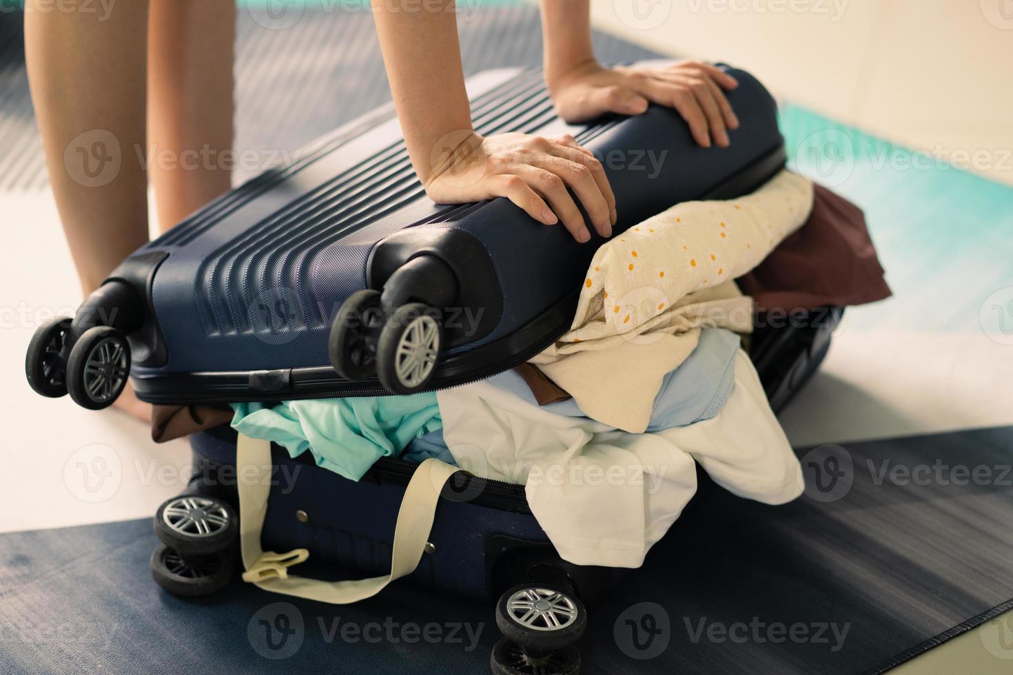 femme asiatique essayant de fermer une valise pleine de vêtements photo