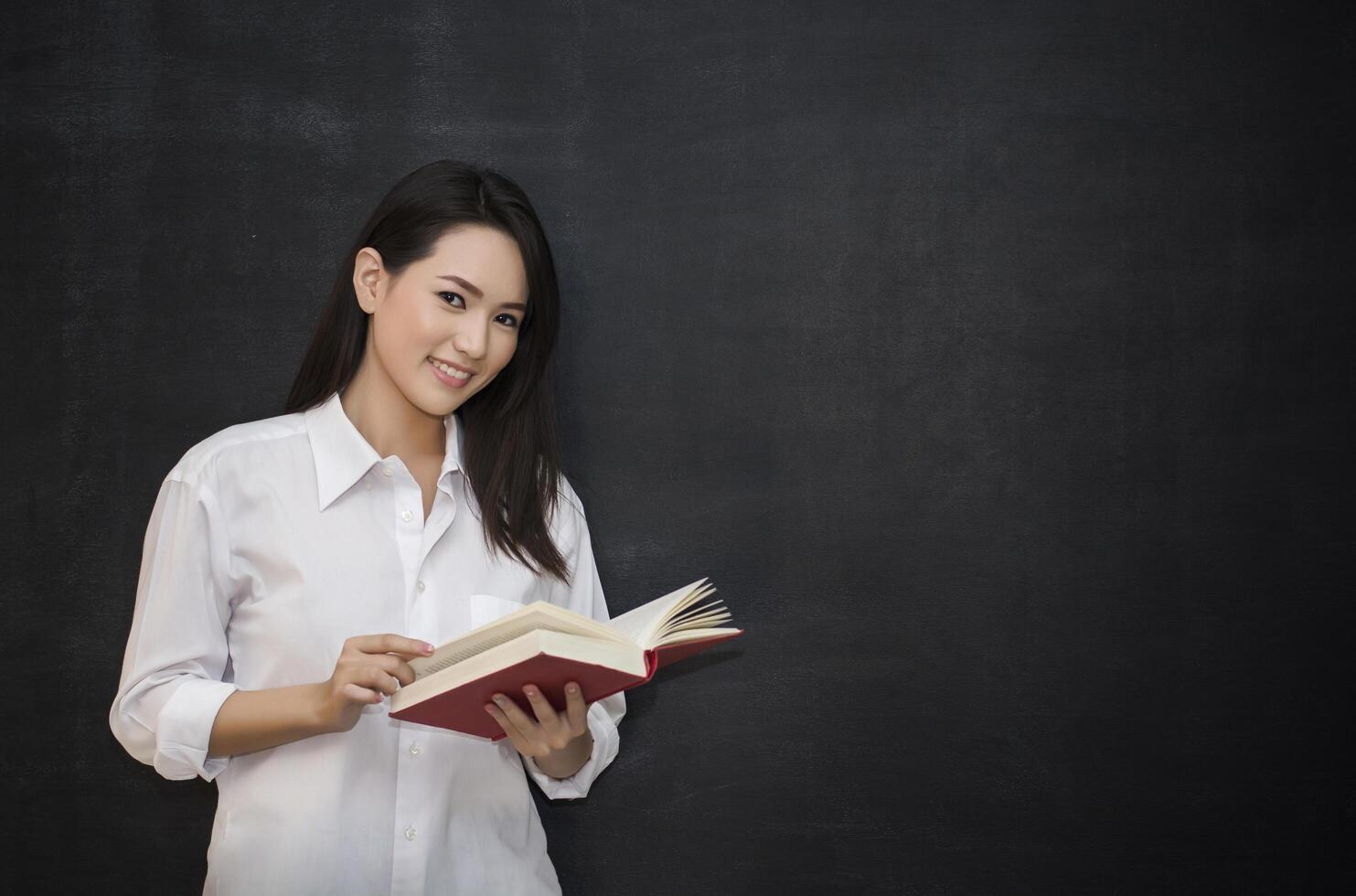 jeune femme asiatique lisant un livre en se tenant debout contre le tableau noir photo