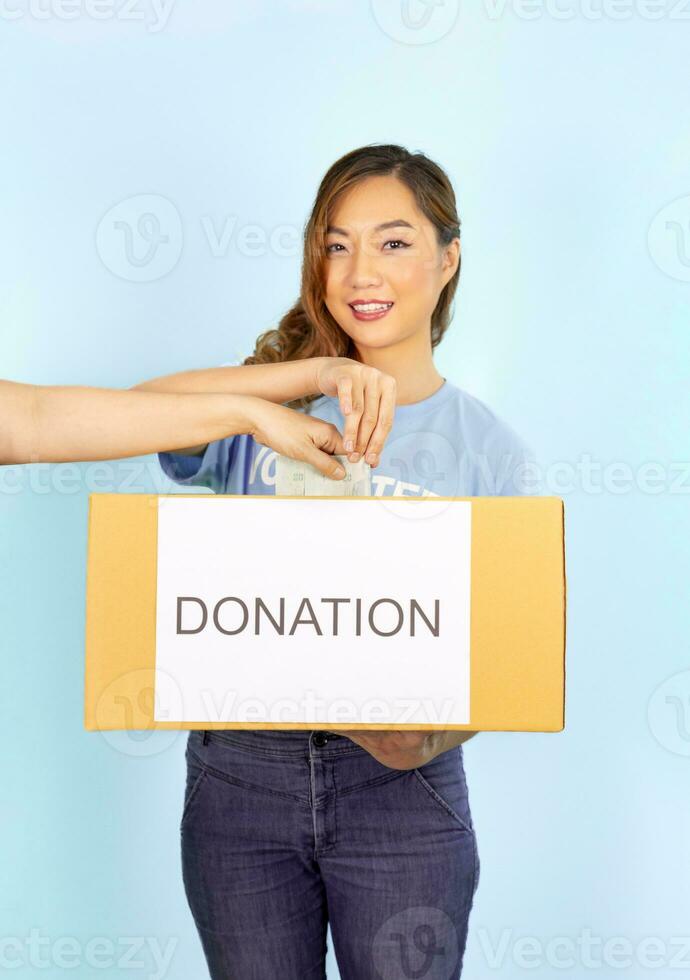 une femelle bénévole porte bleu T-shirt en portant don boîte, femme main donnant billet de banque dans don boîte, isolée sur bleu arrière-plan, sélectif concentrer à mains, charité don financier soutien concept photo