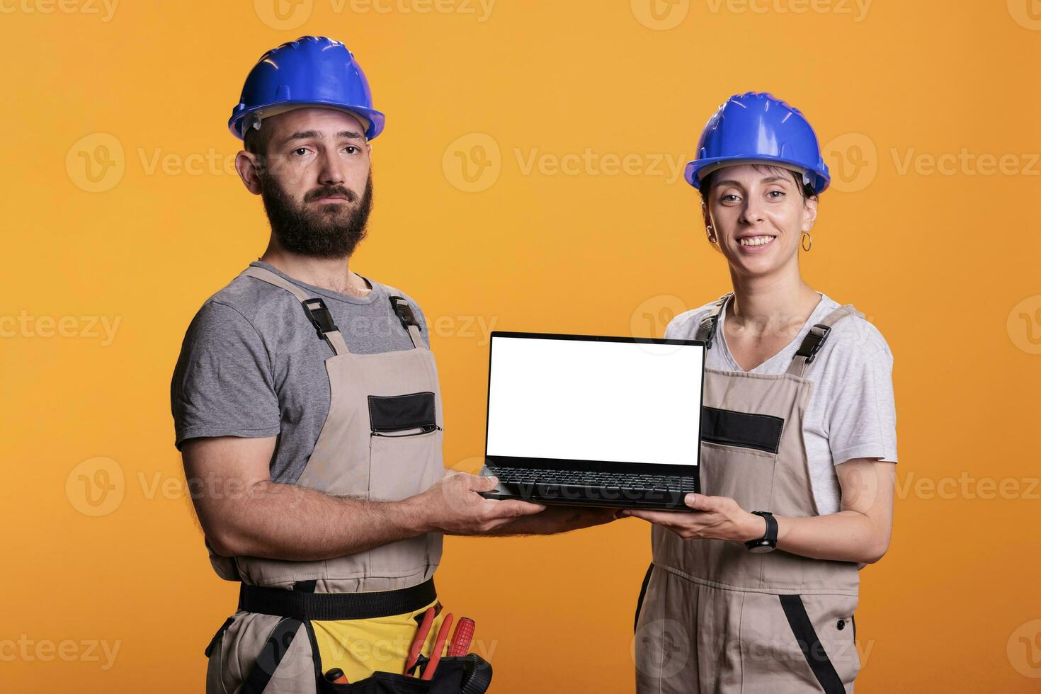 équipe de constructeurs montrant blanc vide écran sur ordinateur portable, portant salopette et casques dans studio. construction ouvriers La publicité isolé fond afficher sur portable ordinateur, Vide maquette. photo