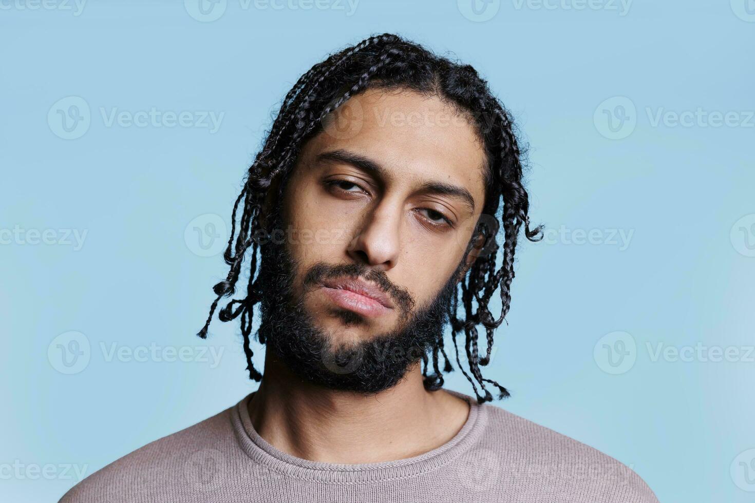 cool sur de soi attrayant arabe homme basculant tête avec sérieux faciale expression portrait. Jeune adulte brunette arabe la personne avec tresses coiffure et décontractée vêtements à la recherche à caméra photo