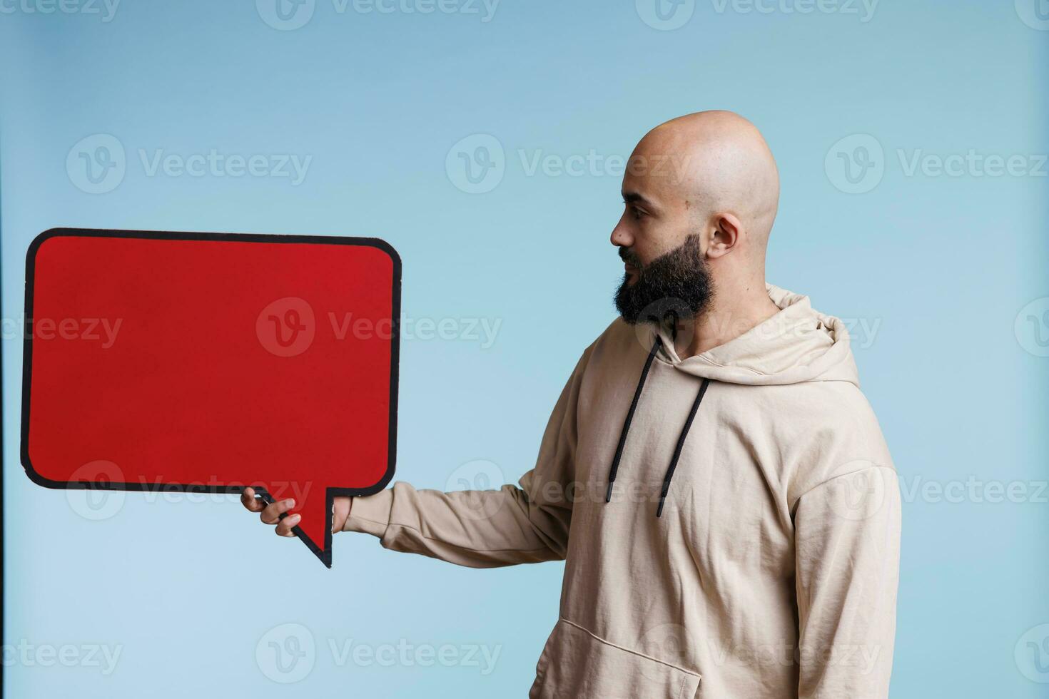 arabe homme La publicité produit avec vide rouge bannière, montrant Cadre pour texte. Jeune la personne en portant Vide dialogue bulle forme avec chape espace pour promotionnel message moquer en haut photo