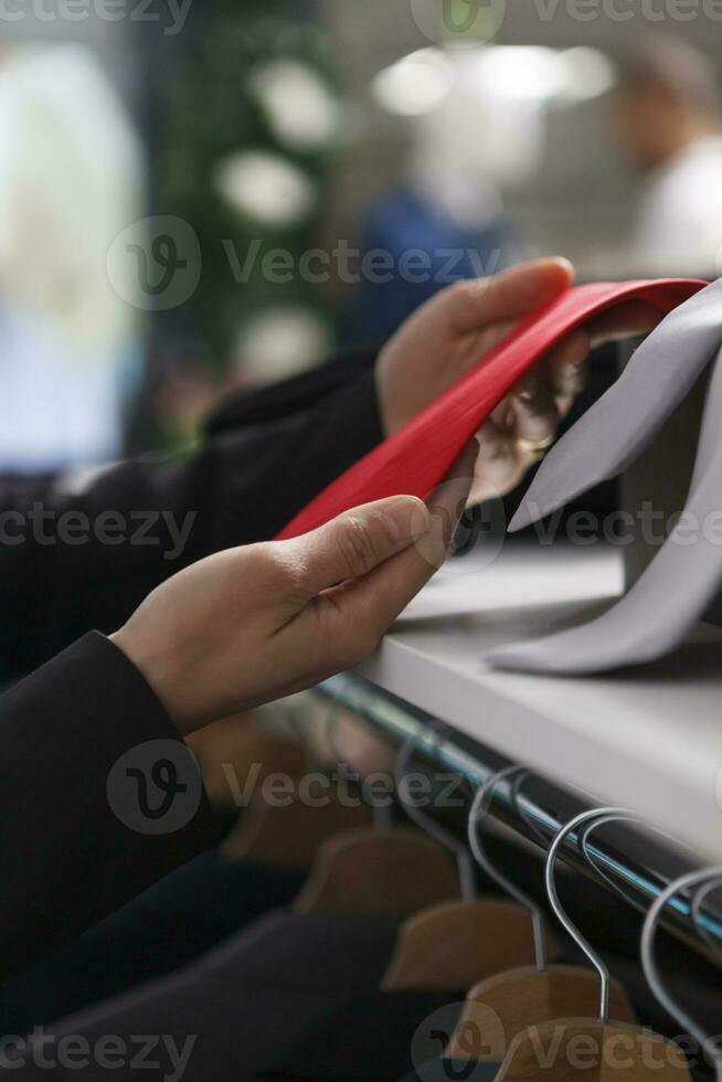 Vêtements boutique femme assistant bras en portant rouge attacher tandis que navigation par accessoire collection pour vente fermer. boutique vendeur mains en portant marchandise tandis que travail dans achats centre commercial photo