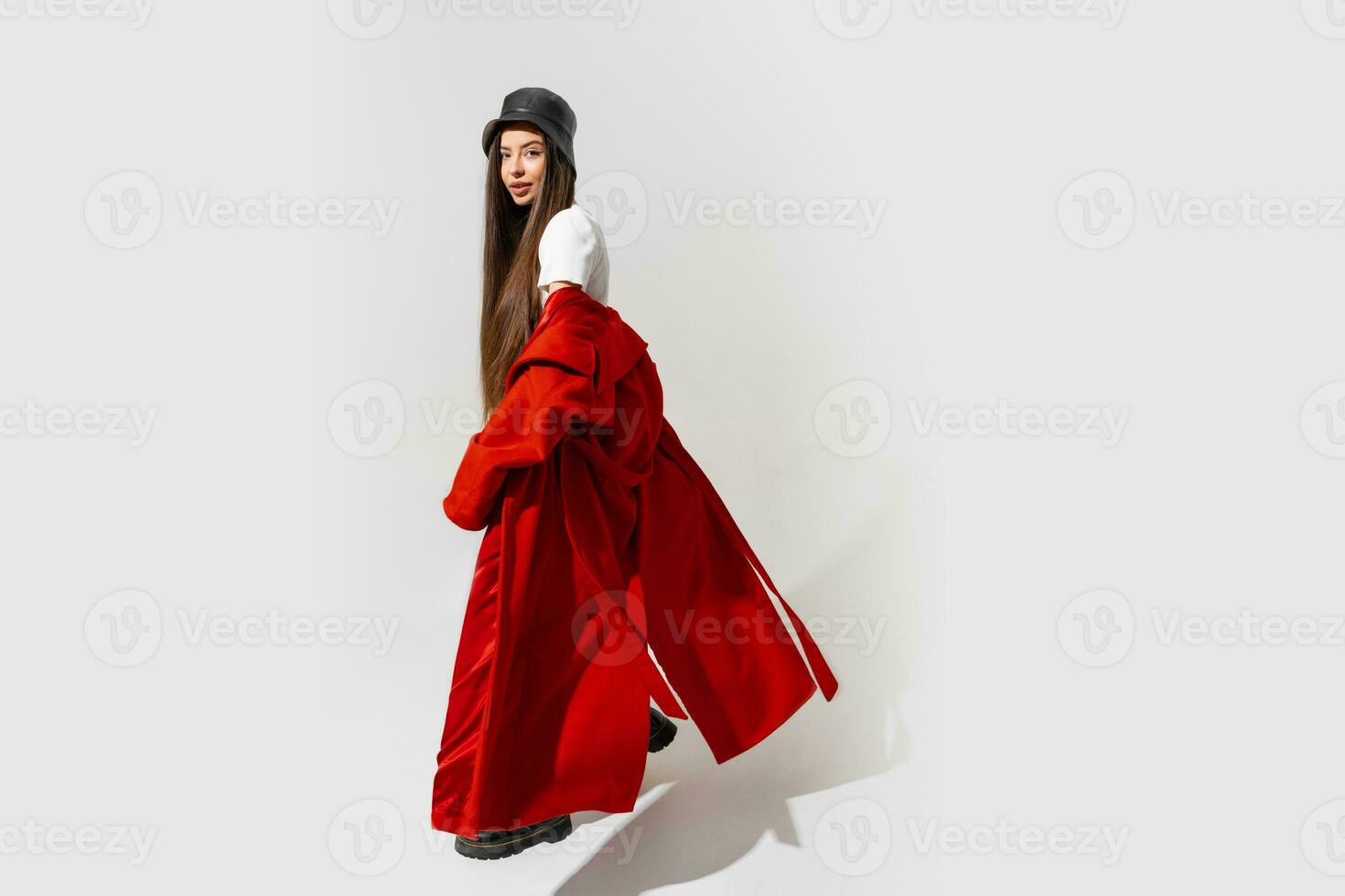 mode studio photo de élégant européen brunette femme dans rouge manteau et noir chapeau posant sur blanc Contexte. branché hiver accessoires. plein longueur.