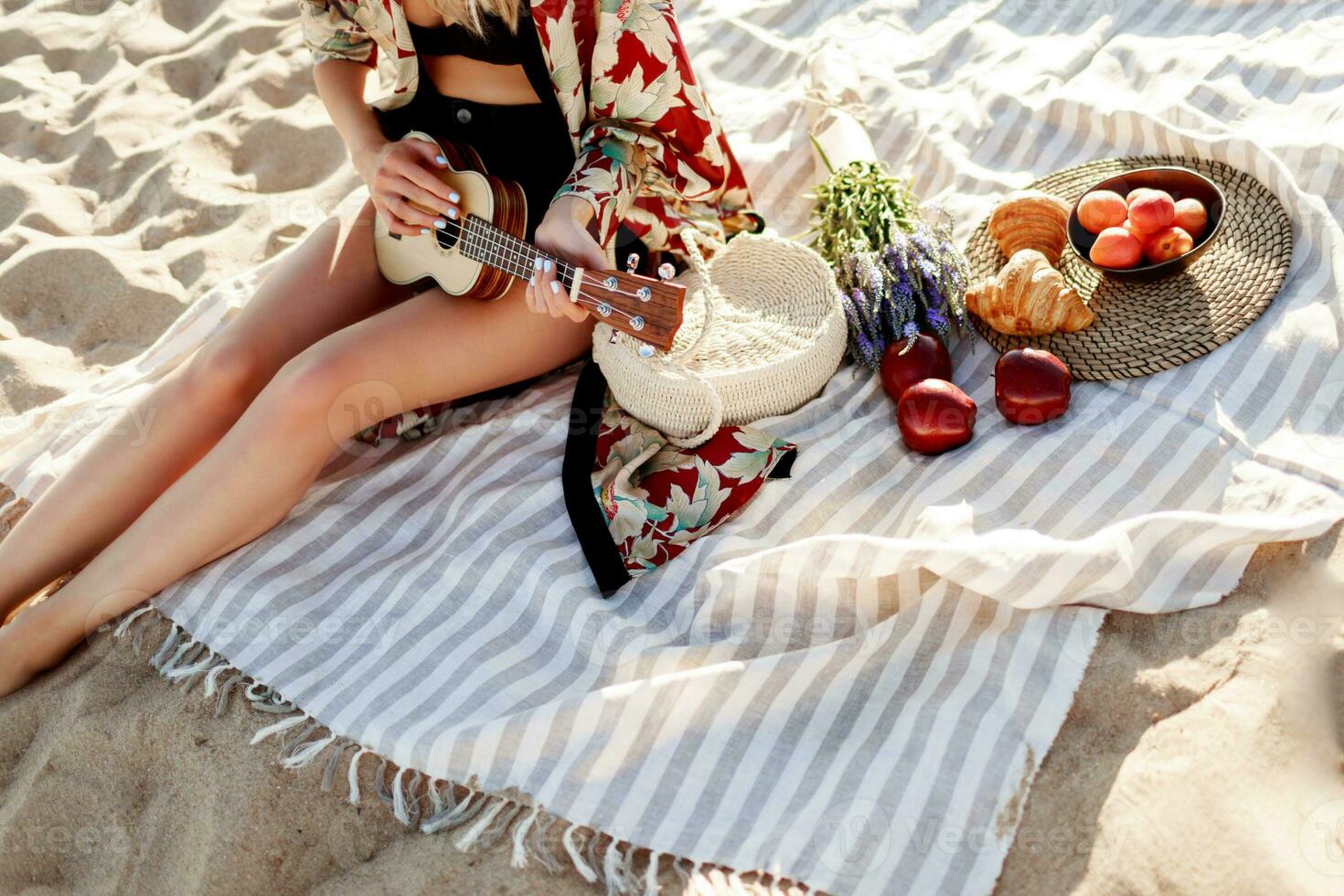 romantique femme dans paille chapeau séance sur couverture sur le plage et en jouant ukulélé guitare. pique-nique, fruits photo