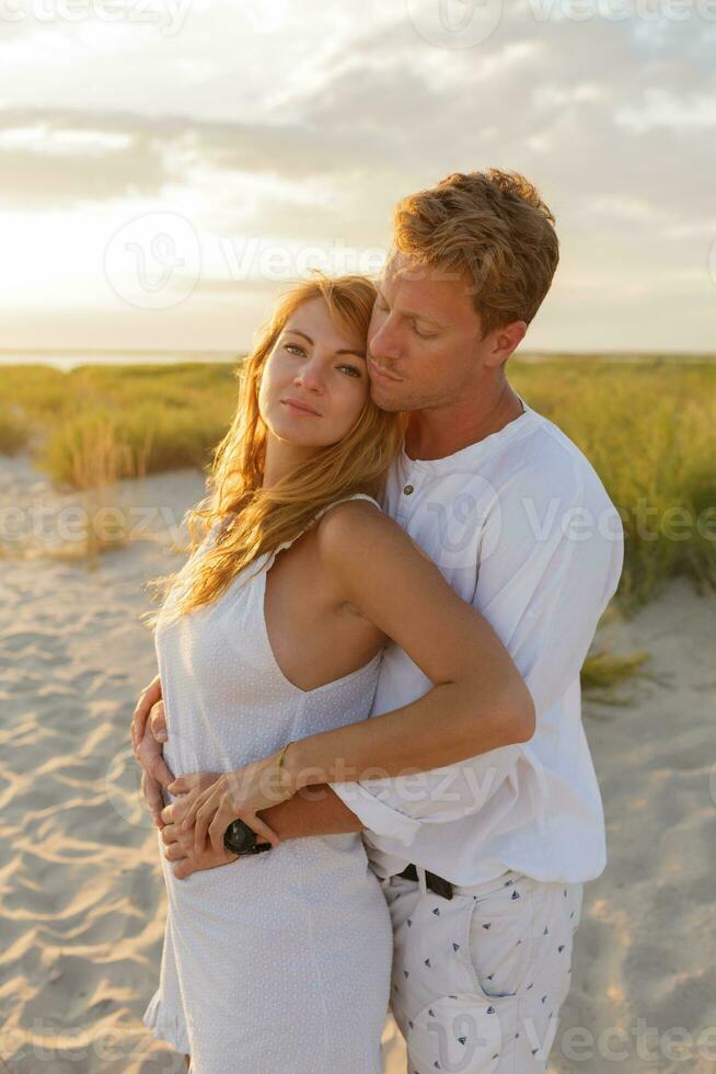 européen magnifique couple embrassement contre le coucher du soleil tandis que sortir ensemble sur le plage. proche en haut portrait de homme et femme ensemble, à la recherche à chaque autre. photo
