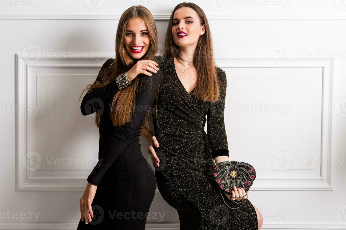 deux Jeune élégant souriant femmes, copains dans soir décontractée tenue ayant amusement sur blanc Urbain mur. brillant faire en haut. photo