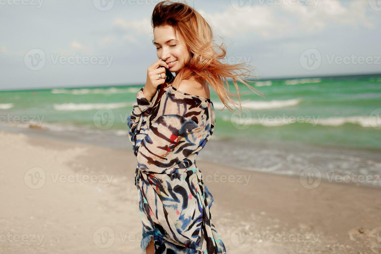 insouciant femme sauter liberté sur blanc sable. bleu océan Contexte. venteux Cheveux. photo