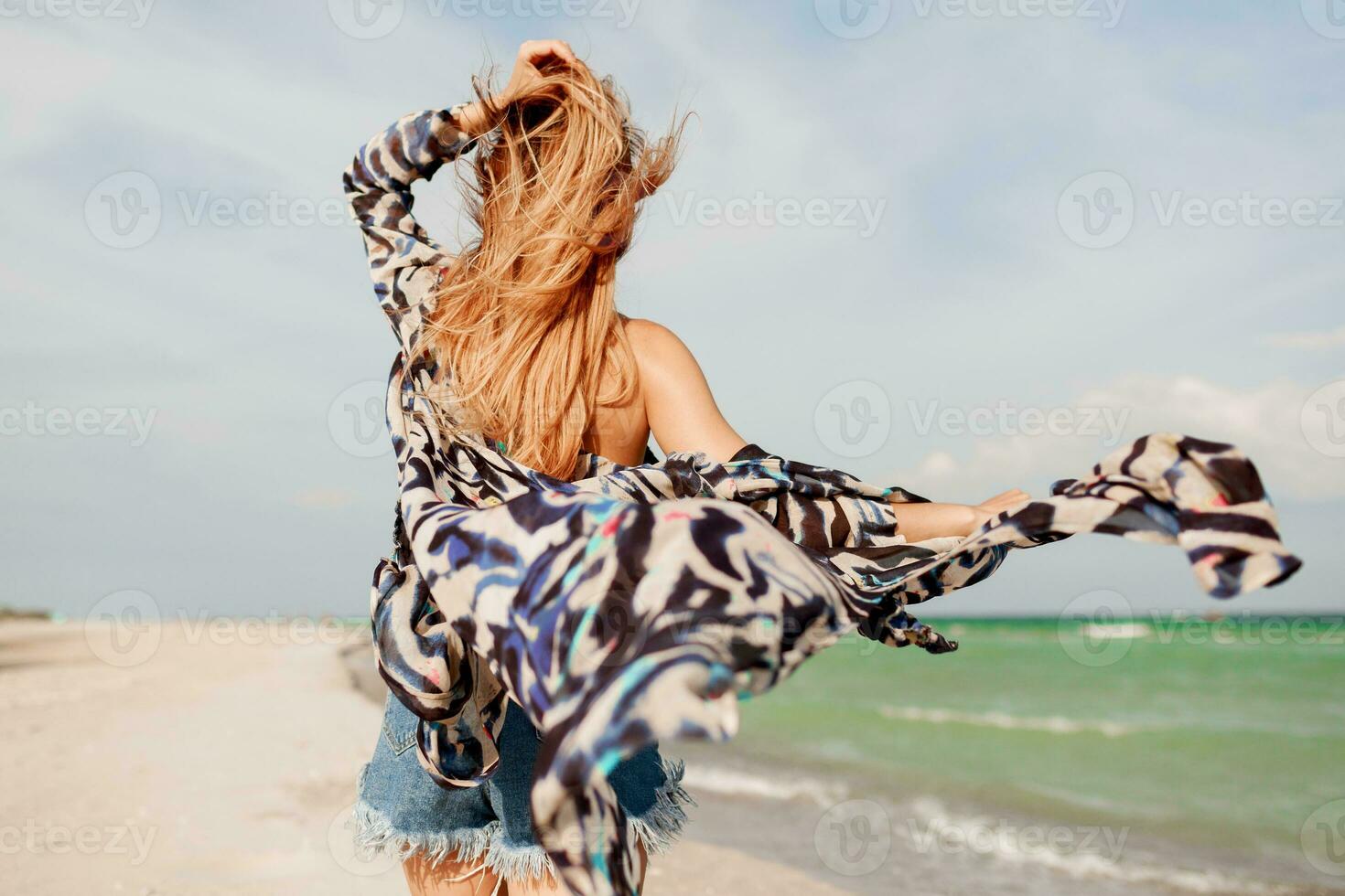 insouciant femme sauter liberté sur blanc sable. bleu océan Contexte. venteux Cheveux. photo