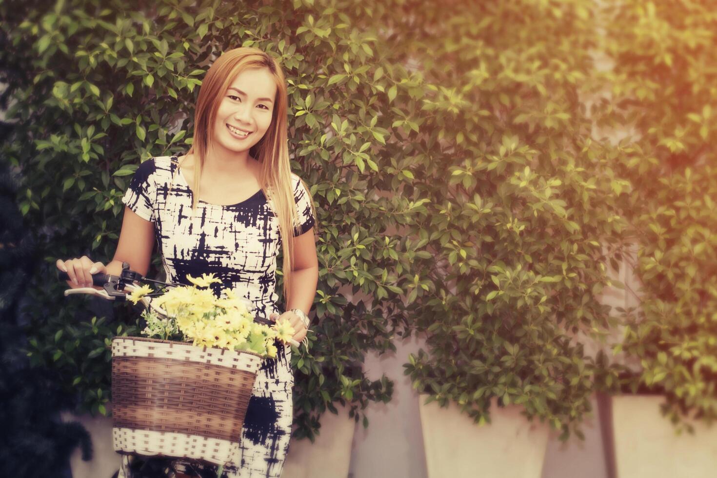 belle femme debout à côté et tenant un vélo avec des fleurs. photo