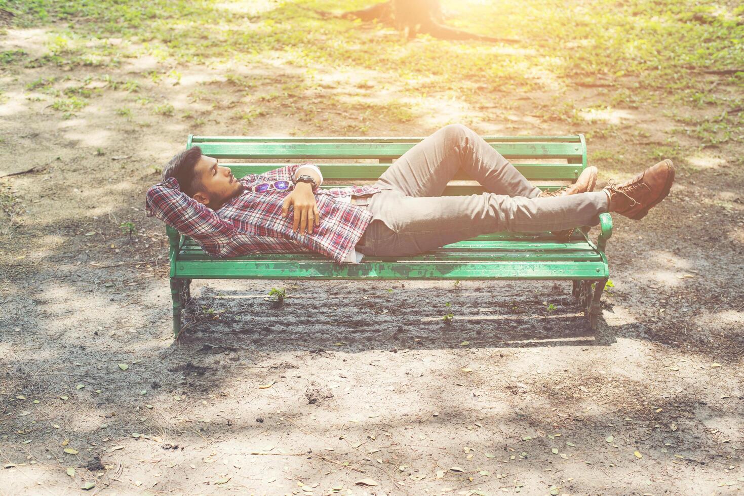 jeune homme hipster allongé sur un banc de parc verdoyant, à l'écart. photo