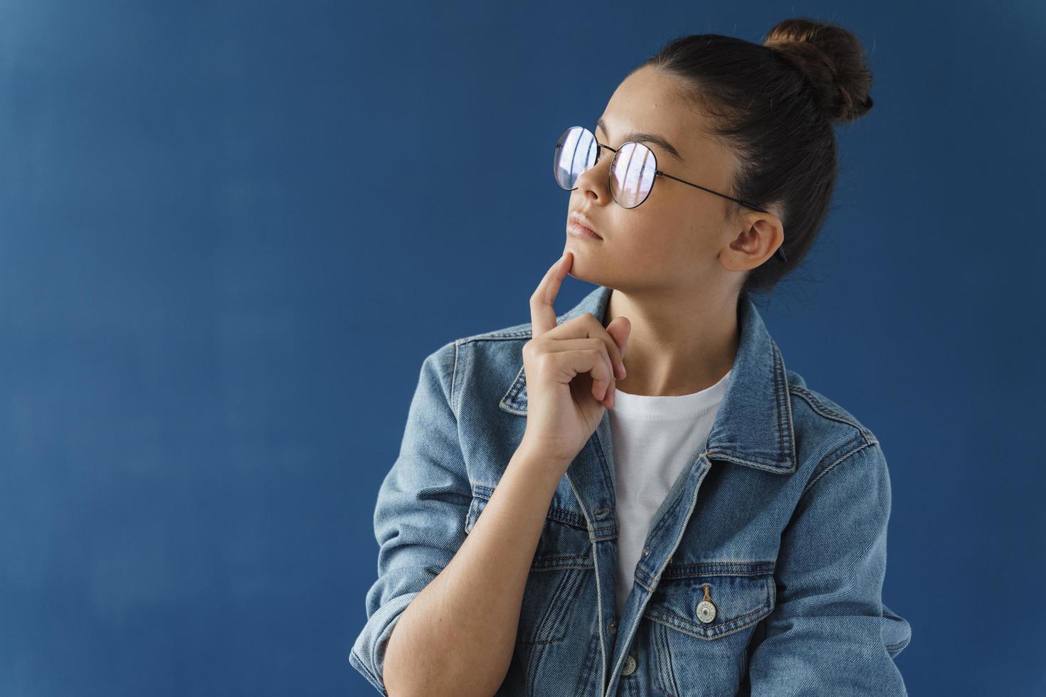 Une adolescente rêveuse et mignonne avec des lunettes touche son menton, détourne le regard photo