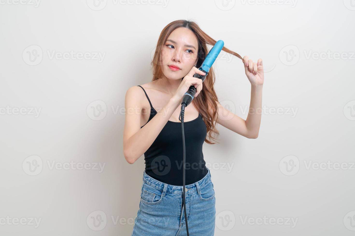 Portrait belle femme asiatique à l'aide d'un bigoudi ou d'un fer à friser sur fond blanc photo