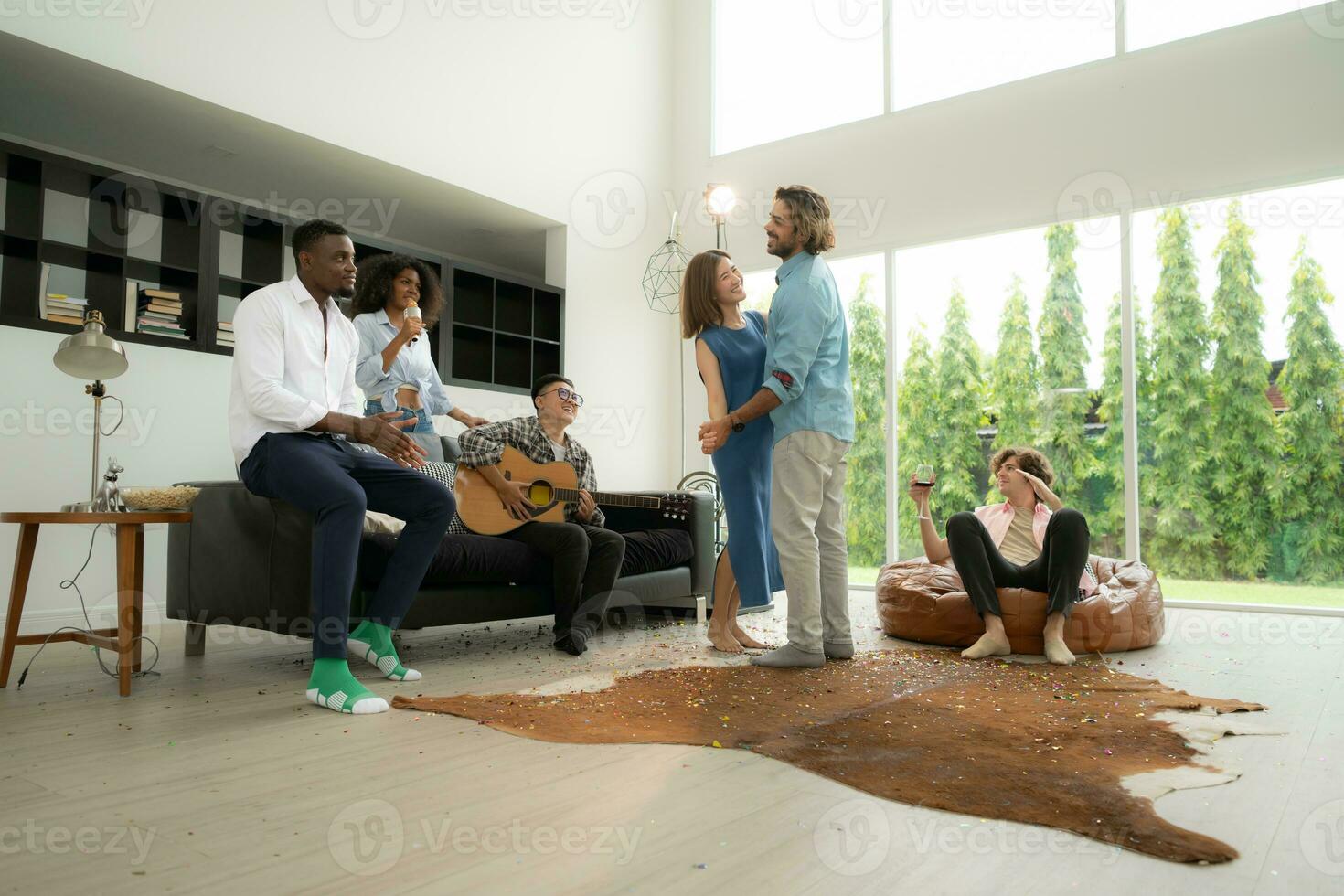 groupe de Multi-éthnique copains ayant amusement à fête par en jouant guitare, en chantant et Danse ensemble à maison. photo