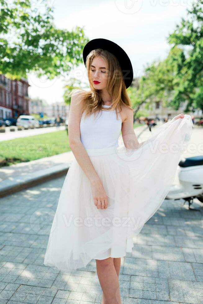 Jeune magnifique blond femme dans élégant printemps décontractée tenue en marchant dans ville. ancien doux Ton image . venteux Cheveux. photo