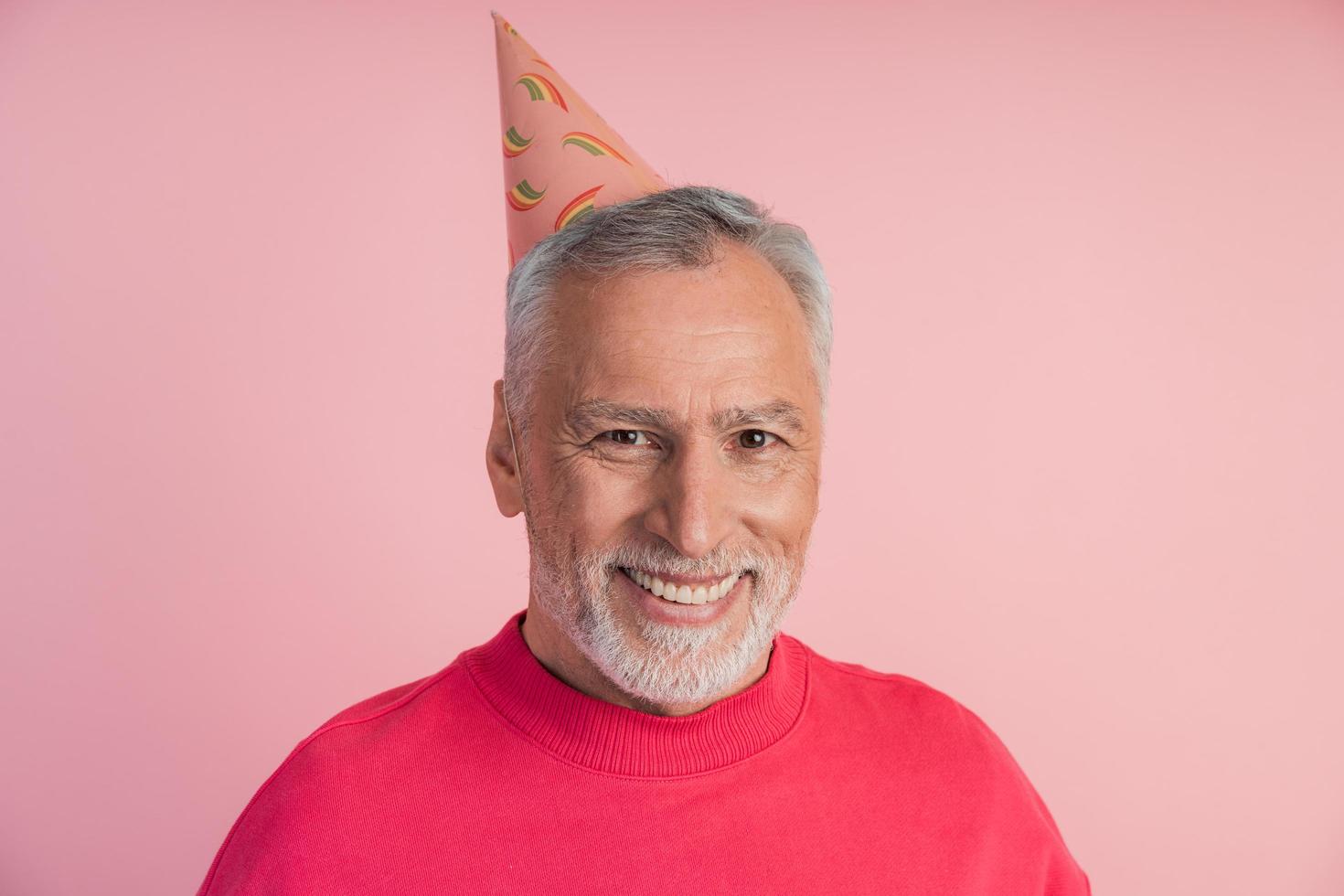 homme gai et souriant dans un chapeau de fête sur fond rose. photo