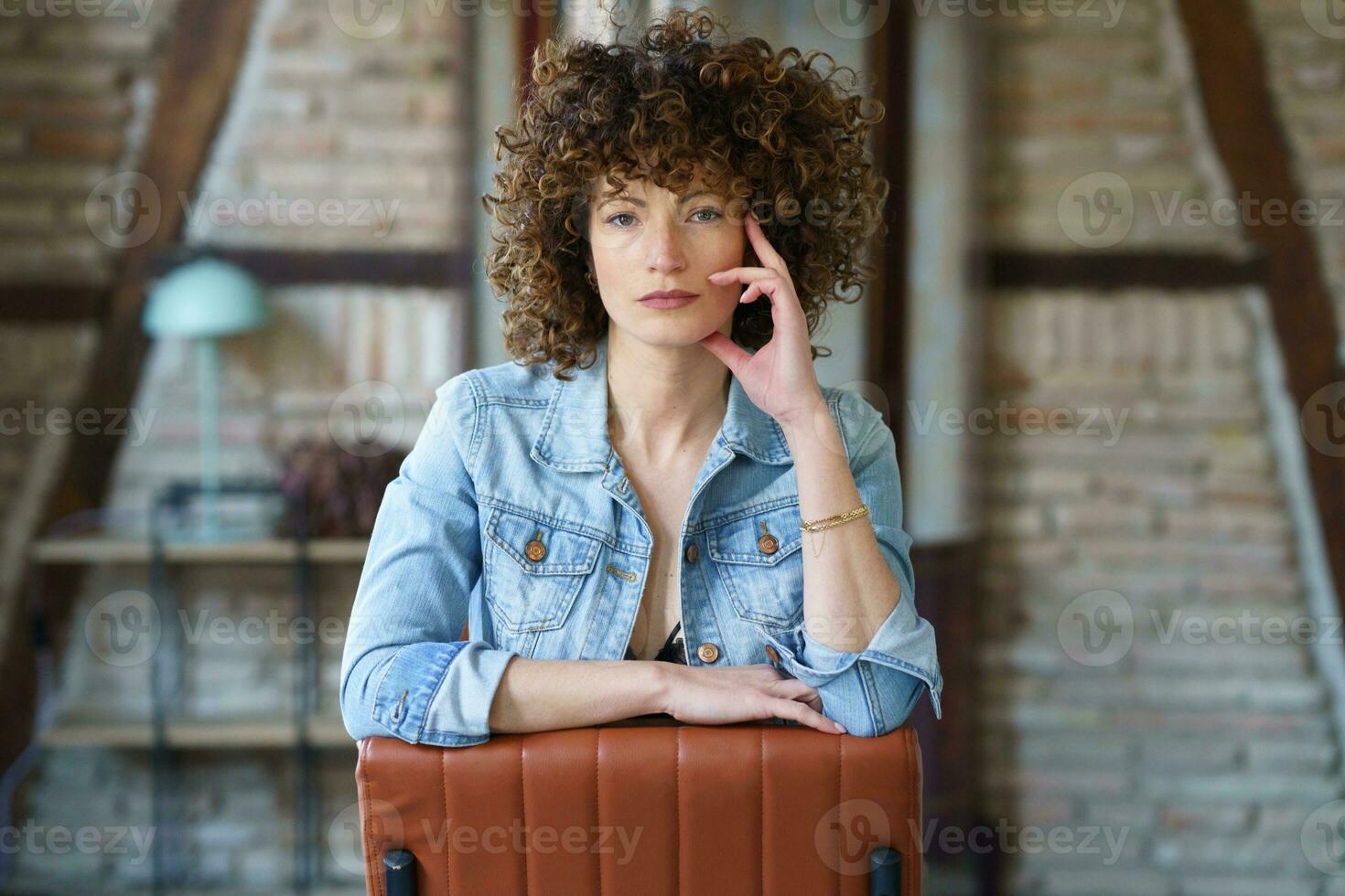 sérieux Jeune femme portant denim veste séance sur cuir chaise photo