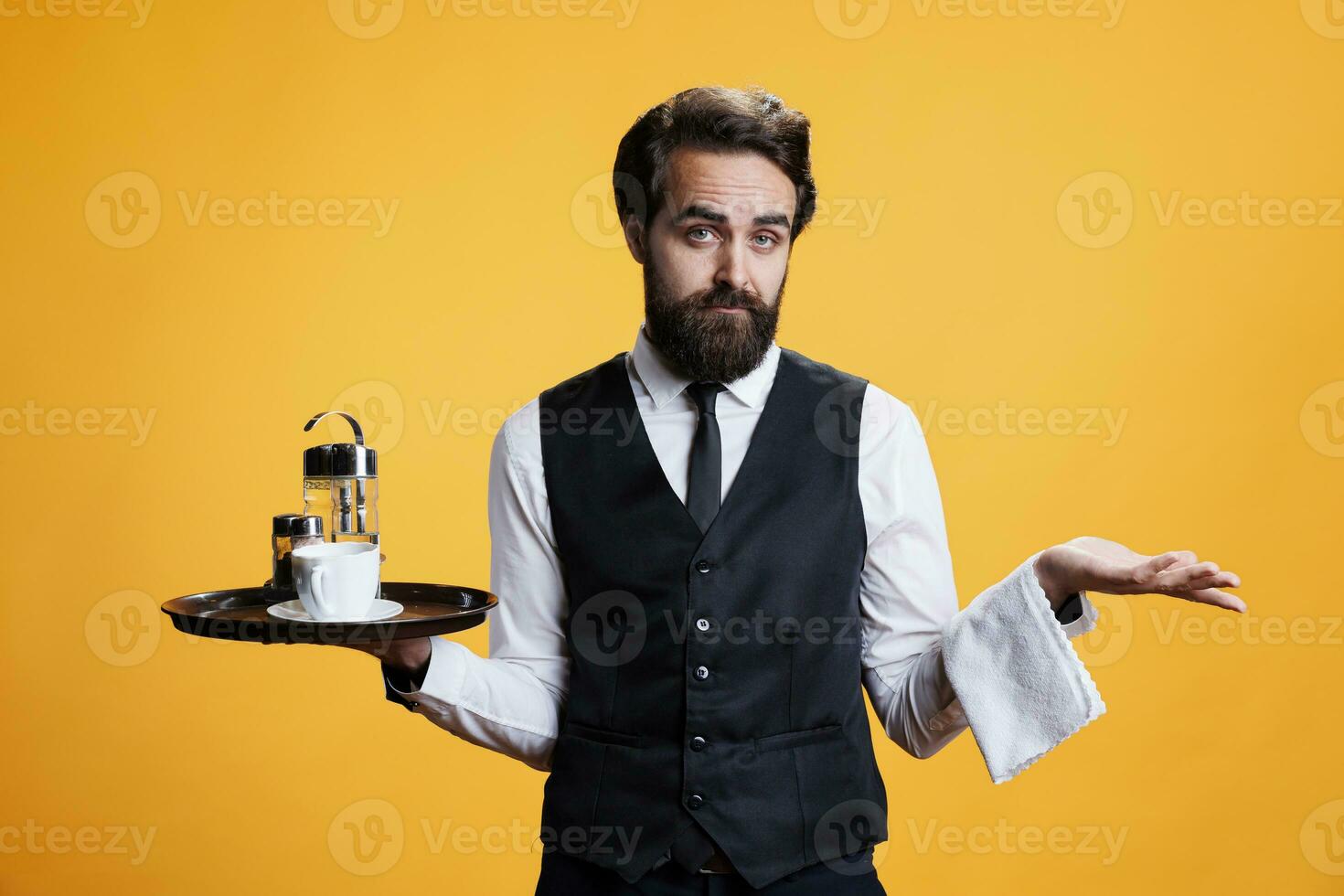 Masculin serveur sentiment incertain dans studio, Faire je ne pas connaître geste et haussant les épaules. restaurant employé agissant Aucune idée et incertain tandis que il est en portant plat dans main, pose plus de Jaune Contexte. photo