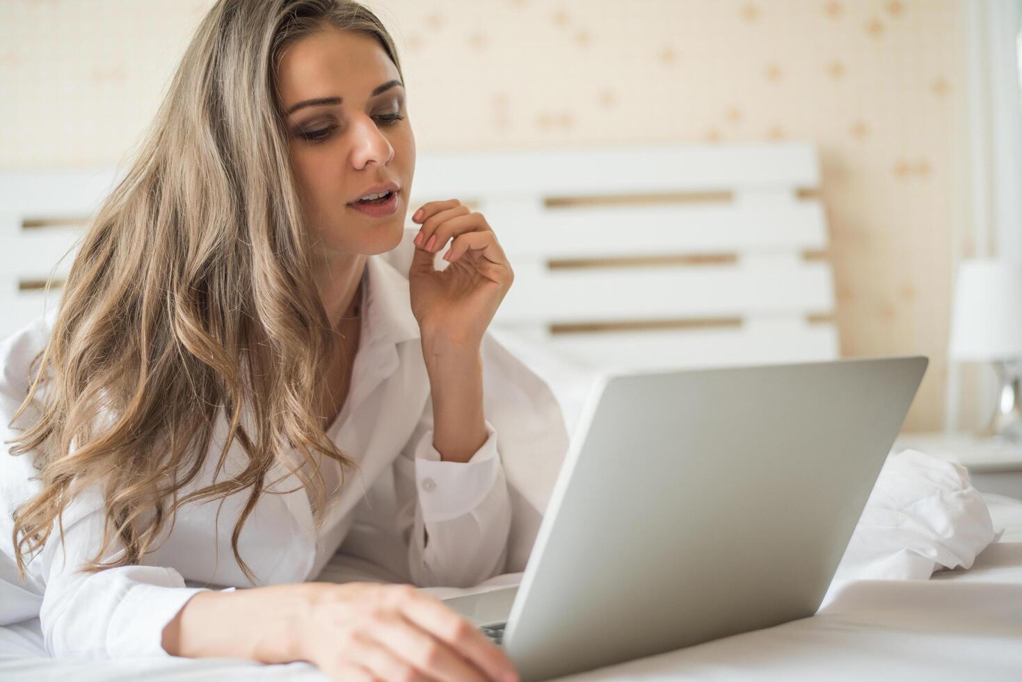 heureuse belle femme travaillant sur un ordinateur portable sur le lit dans la maison photo