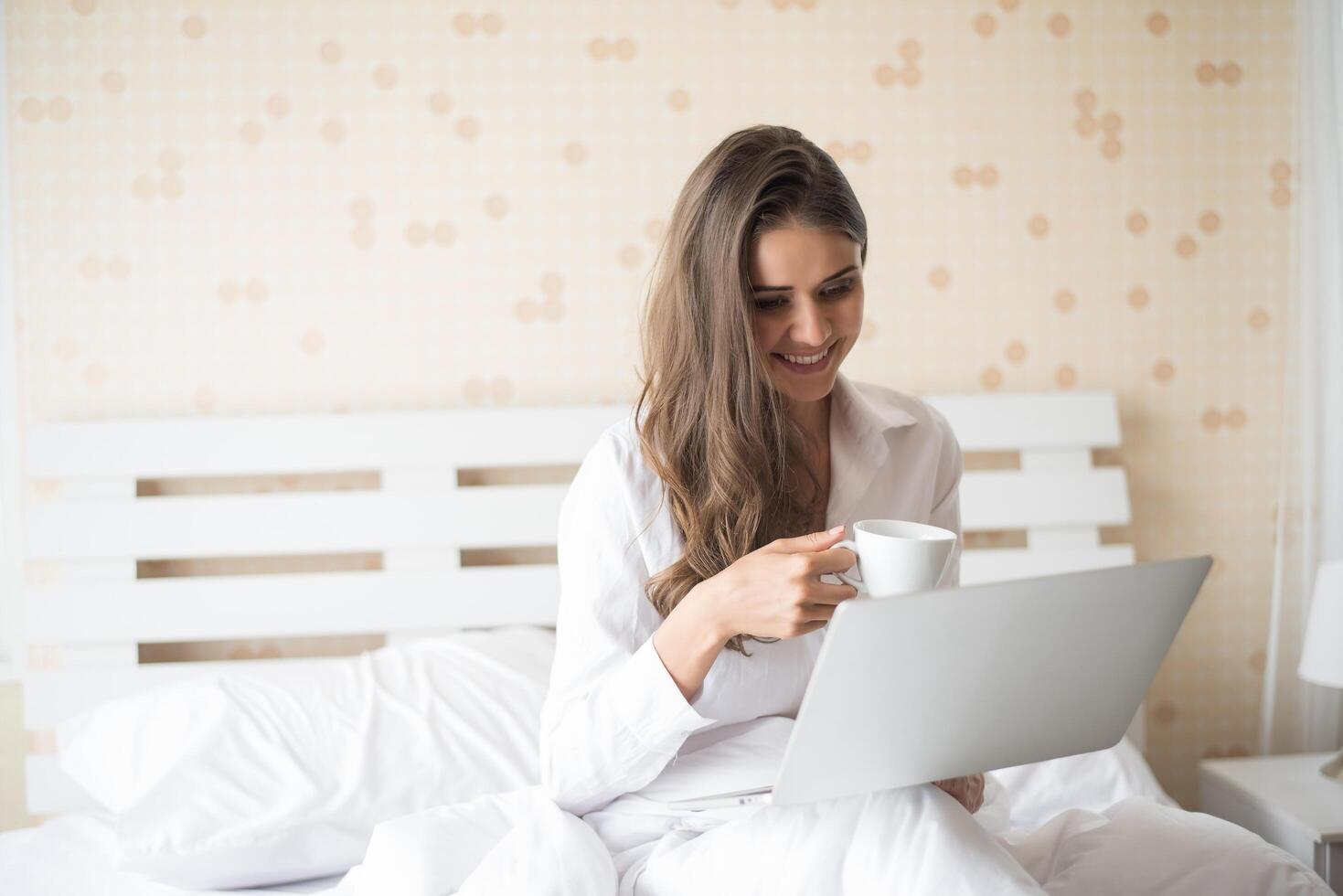 heureuse belle femme travaillant sur un ordinateur portable sur le lit dans la maison photo