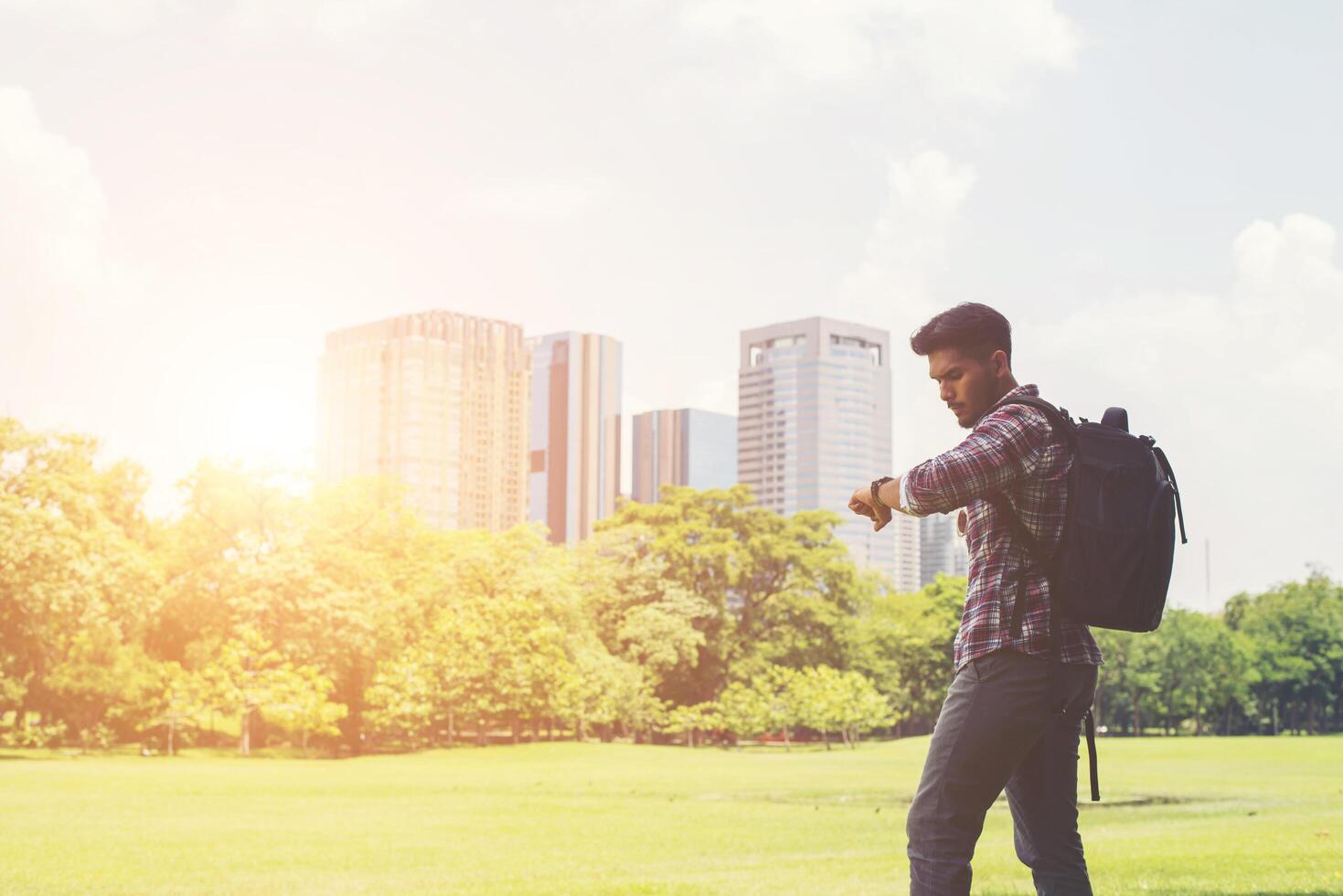 jeune homme hipster regardant sa montre derrière la vue sur la ville depuis le parc. photo