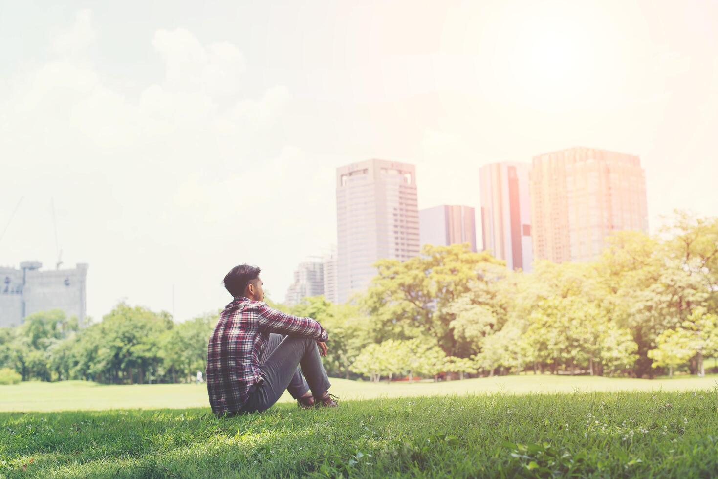 vue arrière du jeune homme de voyage détendu assis sur l'herbe dans le parc. photo