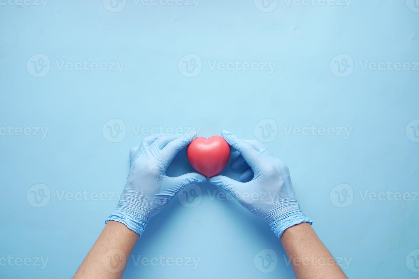 main d'homme dans des gants de protection tenant un coeur rouge sur bleu photo