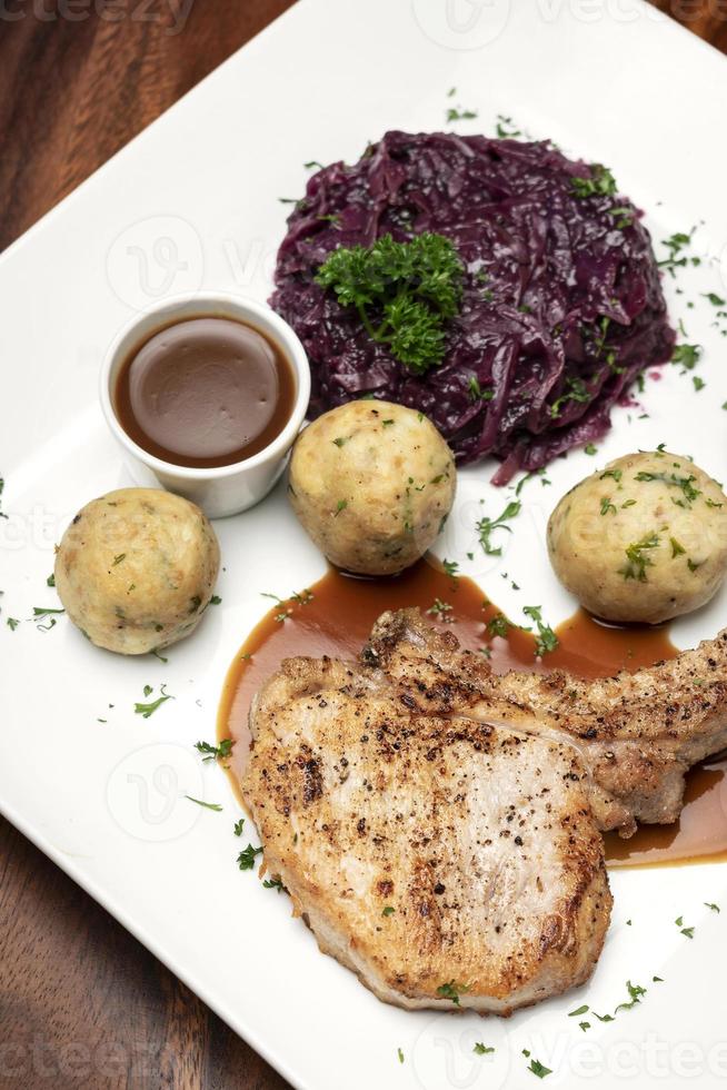 côtelette de porc grillée à l'allemande avec boulettes de pain et repas traditionnel de chou rouge sur table en bois photo