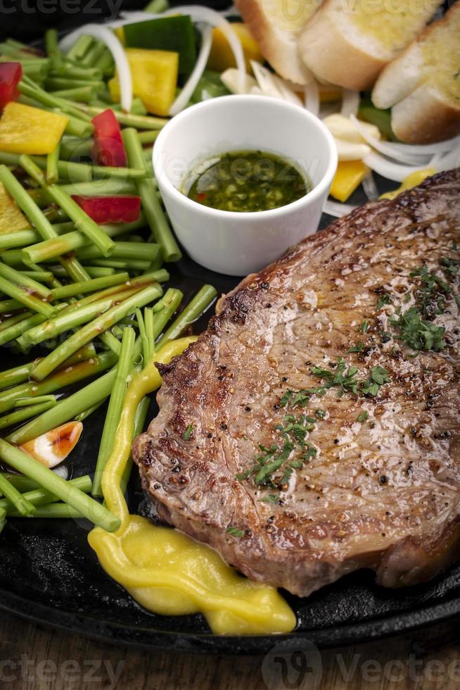 Bifteck de filet de bœuf bio sizzler sur plaque chauffante assiette de repas avec légumes mélangés et sauce chimichurri photo