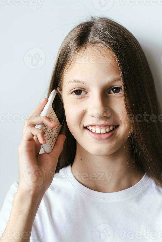 souriant adolescent fille parlant sur une blanc bouton téléphone verticale vue photo